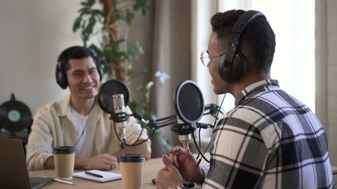 Businessmen talking and recording audio podcast, sitting at table while broadcasting online spbd. Two young men talk in front of microphones and look with smiles, record and use equipment at desk in