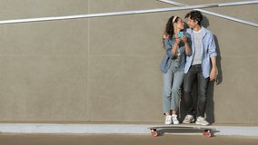 Happy hipsters couple on date. Stylish girl laugh with smartphone in hands. Man and woman spend time outdoors having rest after skateboarding, laugh from funny videos in social media or mobile apps - Powered by Shutterstock - Get 15% off with code: PIKWIZARD15