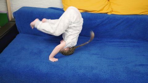 Child girl plays in room, does somersaults on sofa in room. Little girl have fun doing somersault at home, sports game. Acrobatic exercises kid, childhood. Kid does somersaults, rolls over. Family