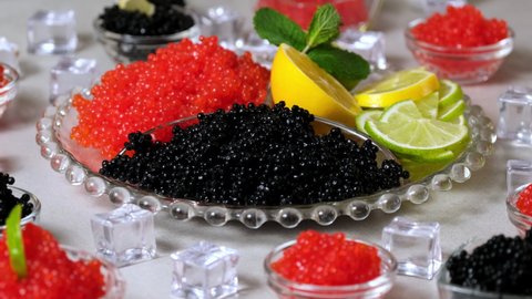 Caviar. Red and black caviar in dishes. Elite salmon caviar and black Beluga sturgeon salted roe on ice. Appetizing snacks on table with lemon, lime. Delicatessen. Gourmet food. Rotating