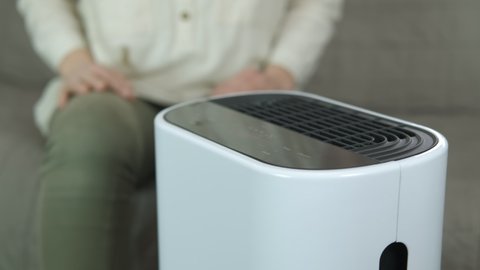 Smart air purifier and pollution. A view of working digital air purifier on the table by the relaxing woman on the sofa.