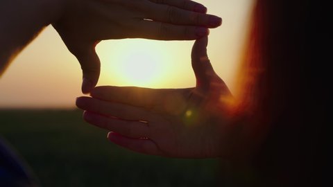 Sees like in movies. Hands of a young female director cameraman making frame gesture at sunset. Concept of seeing world as different. Business planning. Girl shows her fingers frame symbol in sun.