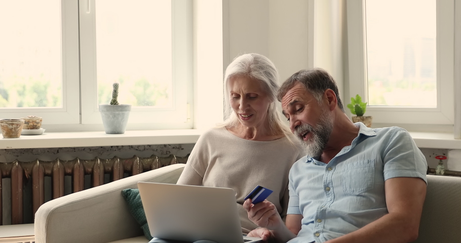Older couple sit on sofa with laptop hold debit card buy furniture for new house, make purchase online use electronic retail services, pay for medical insurance through secure e-bank. Shopping concept Royalty-Free Stock Footage #1086568688