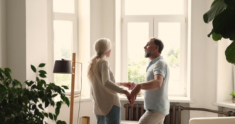 Happy active older spouses spend free time, carefree leisure together listen favourite song, holding hands dancing at home. Mature couple in love enjoy romantic date move to the music have fun indoor Royalty-Free Stock Footage #1086568760
