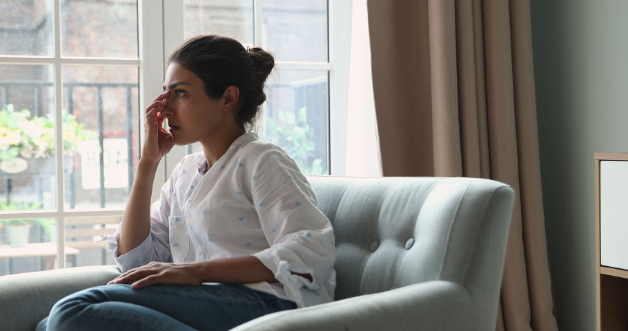 Worried Indian woman sit on armchair looks concerned, feels depressed due life troubles break up, divorce, thinks about abortion suffering alone at home. Psychological problem, regret, mistake concept Royalty-Free Stock Footage #1086568772