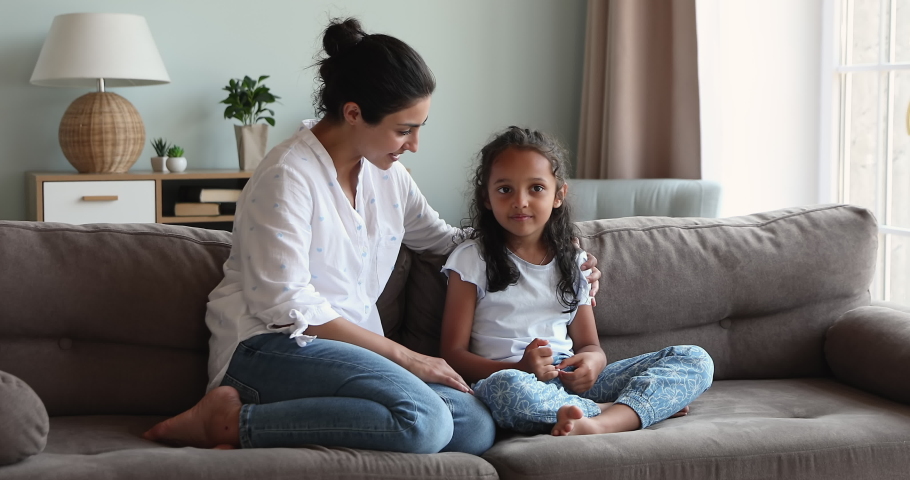 Young loving Indian mom talking to little 6s daughter seated together on sofa at home. Preschool kid and mother having warm, trustworthy conversation, good relation. Understanding, family bond concept Royalty-Free Stock Footage #1086568811