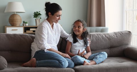 Young loving Indian mom talking to little 6s daughter seated together on sofa at home. Preschool kid and mother having warm, trustworthy conversation, good relation. Understanding, family bond concept