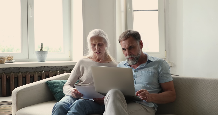 Older couple sit on sofa with laptop, reviewing expenses, learn documents from bank about debt, overspending, having financial problems feeling stressed. Bankruptcy, lack of money to pay bills concept Royalty-Free Stock Footage #1086568838