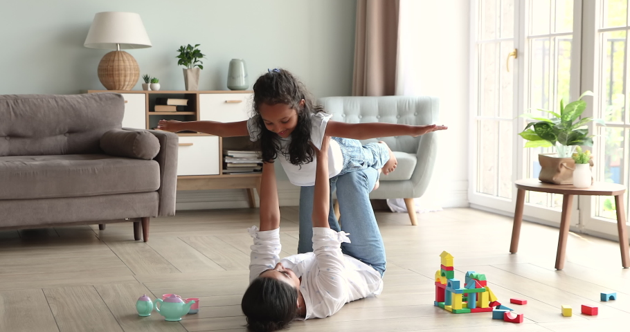 Loving Indian mom raise on outstretched arms her cute little daughter, family play together indoors dreaming about travel feeling carefree and happy. Happy motherhood, games with kids at home concept Royalty-Free Stock Footage #1086568886