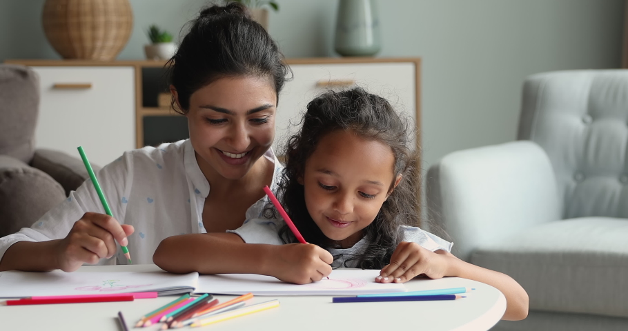 Close up beautiful Indian woman her adorable small 6s daughter drawing in sketchbook using colored pencils. Loving mother develop her child, enjoy conversation, hobby, creative pastime at home concept Royalty-Free Stock Footage #1086568892