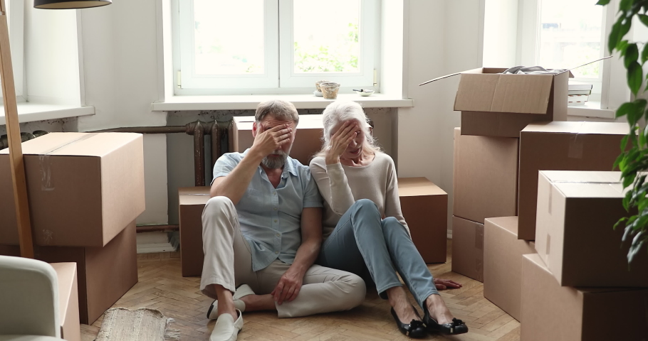 Older couple sit on floor near heap cardboard boxes with personal stuff looks stressed, upset due or bank debt and eviction kick out from home, take break at hard long relocation move in day concept Royalty-Free Stock Footage #1086568904