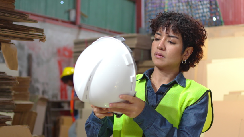 Selective focus of a young pretty short-haired Asian female factory worker in a safety vest standing wearing a helmet on her head to prevent work hazards, prepare well before starting work in factory. | Shutterstock HD Video #1086570113