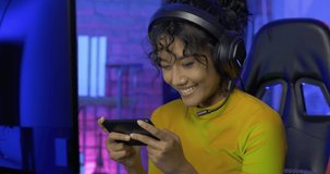 Young woman gamer using smartphone and play in online video game. She playing online games with neon lights background.