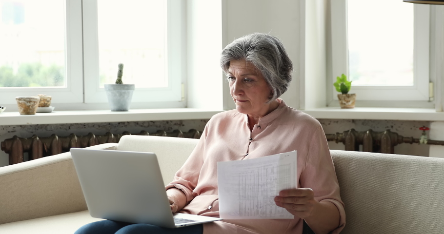 Older upset woman sit on sofa put wireless computer on laps, check utilities rates, experiences problems with e-bank app while pay bills online. Financial trouble, difficult to use modern tech concept Royalty-Free Stock Footage #1086570806