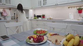 Woman cooking festive dinner preparing appetizers in the kitchen, female hands putting pickles and olives in serving dish on kitchen counter. High quality 4k footage