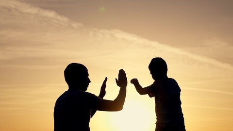 Happy family in park. Father and son boxing in park at sunset. Silhouette of family at sunset. Father helps his son to box. Family box. Sporty happy family concept. Father and son boxing in park