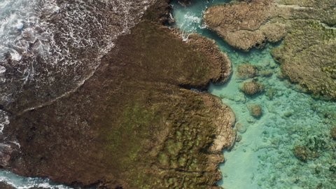 Dynamic aerial footage of brown reef with azure water covered by waves crashing into white sea foam water. Copter footage of tidal surf washing rocky ocean shore. Drone shot of stone and water texture