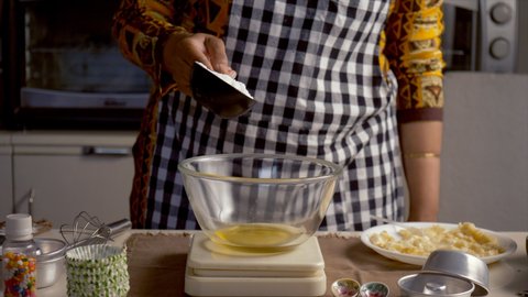 A young Indian chef adding flour in a glass bowl for making cake batter. A plate of butter with a spoon kept on the kitchen counter - cooking ingredient, tasty dessert, professional baker