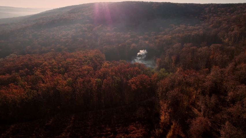 Top view of the autumn reserve, with a house in the forest. Smoke comes out of the chimney.