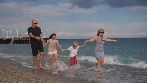 A happy family of 4 people are enjoying a walk along the seashore.