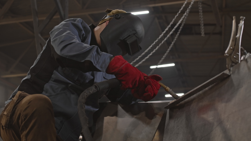 Low angle medium long of unrecognizable worker wearing helmet, welding metallic object indoors | Shutterstock HD Video #1086583571