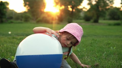 summer, vacation, nature, happy childhood - one small toddler preschool child smiling kid girl in pink hat sit posing looking at camera play with big inflatable in park on meadow at sunset fresh air