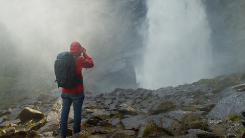 Photographer with backpack takes picture of epic waterfall