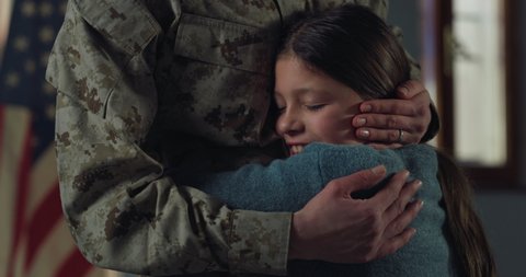Cinematic close up shot of young female soldier mother in camouflage military uniform is hugging emotionally and caressing with love and affection her daughter just turn back home after mission.