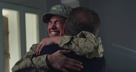 Cinematic shot of young female soldier caught in camouflage military uniform and cap is hugging emotionally her grey hair father and cries of happiness just turn back home after mission.