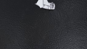 Sailing boat on dark water. Flight over white boat.Yacht from drone. Yachting video. Yacht from above. Wind white sails at passenger boat. Straight down birds eye view from drone.
