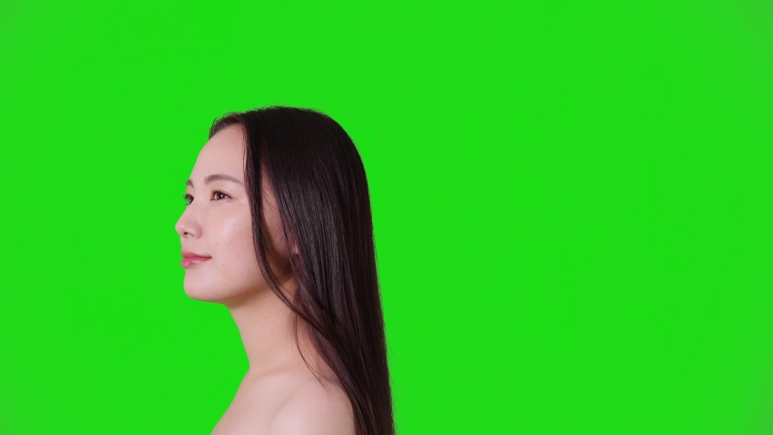 Young asian woman blowing her hair. Hair care concept. Green background for chroma key composition.