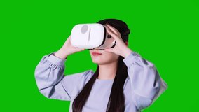 Young asian woman wearing VR goggles. Green background for chroma key composition.