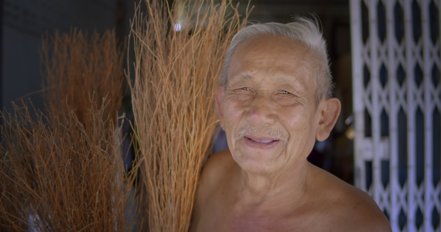 Smiling Asian male farmer who is an elderly person makes brooms from the grass that has many names called Paddy's lucerne, Queensland hemp , Arrowleaf sida , Common sida , Cuba juite for extra income. Royalty-Free Stock Footage #1086602846