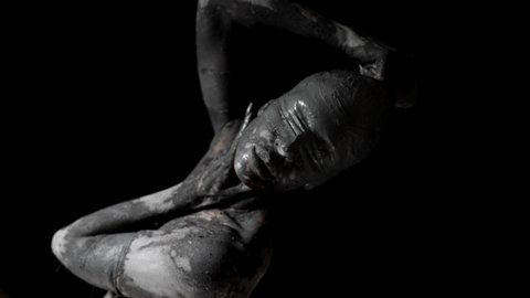 strange woman covered by grey clay and blindfolded in darkness, mysterious life statue