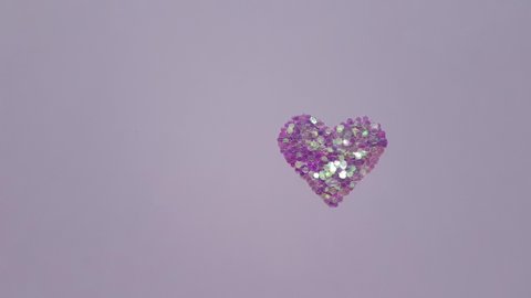 Pale violet heart made of sequins on a purple table.