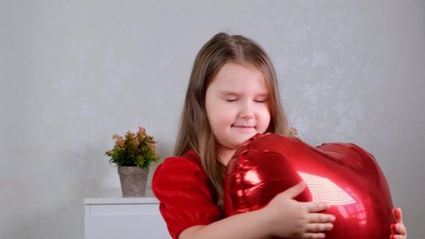 little cute girl in a red dress holding red heart-shaped balloons in her hands concept of valentines day