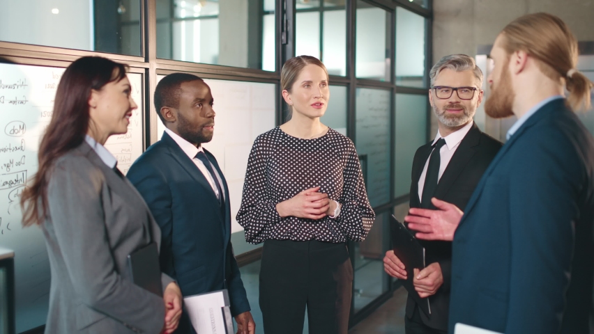 Successful Caucasian blonde business woman communicates with her subordinates standing in office and hands out tasks to work on new project.