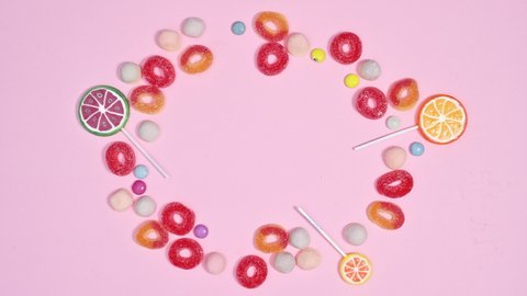 6k Sweet gummy candies, chocolate candies and lollypops appear in circle making frame on pastel pink background. Stop motion animation flat lay