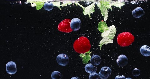 Fresh Blueberry, Raspberry, and Mint Splashing into the Clear Water. Colorful Berries falling slowly in water with bubbles on Dark Background. Summer Fruits. Healthy Food. Vitamins.