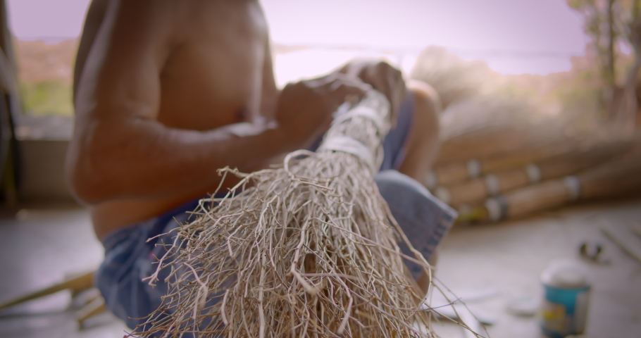 Asian male farmer who is an elderly person makes brooms from the grass that has many names called Paddy's lucerne, Queensland hemp , Arrowleaf sida , Common sida , Cuba juite for extra income. Royalty-Free Stock Footage #1086610079