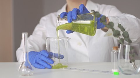 Woman scientist pouring yellow liquid in flask. Scientific cosmetology experiment. Close up.