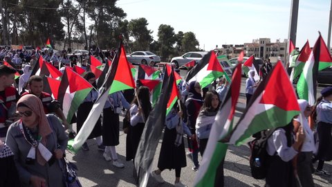 RAMALLAH, WEST BANK – NOVEMBER 11 2021: School girls (some wearing veils, or face masks) carry Palestinian flags through streets of Ramallah, during commemoration of Yasser Arafat's death anniversary