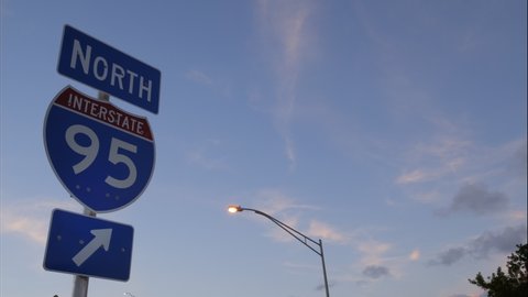 I-95 North sign with arrow pointing to the right against sky after sunset with illuminated street light and wispy clouds moving overhead in a time-lapse