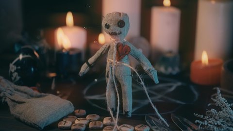 Voodoo doll on table with magical attributes in process of occult ritual and burning candles