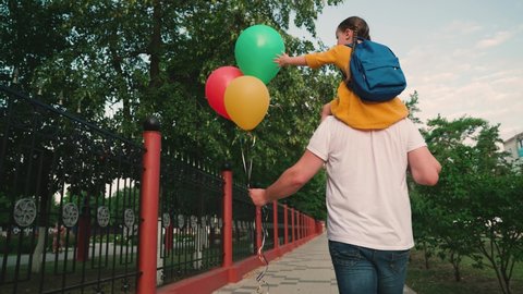 Little daughter plays on shoulders of her father, walk in park with balloons. Holiday is birthday of daughter, walk of father and child along street with multi colored flying balls. Family holiday