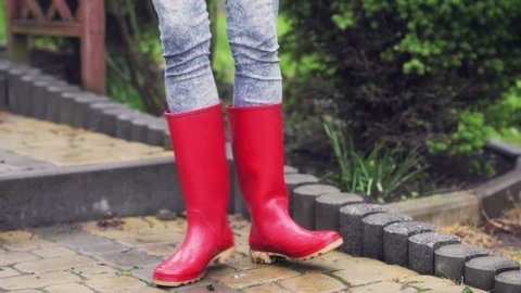 Woman dancing on pavement and wearing red rain boots
