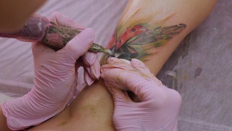 A close-up view of a professional woman tattooist who is tattooing on the leg of a young girl. Hands of a tattooist. Tattooist makes a tattoo.