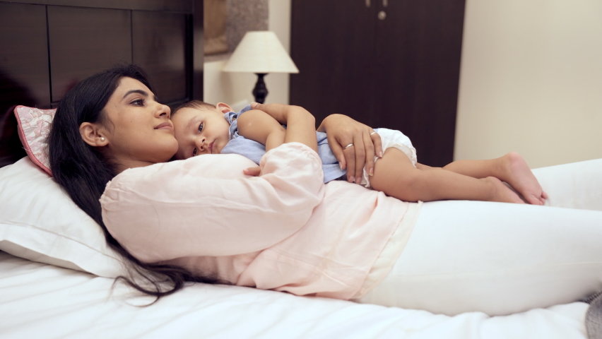 An affectionate Indian mother patting her little daughter to sleep at night. A pretty babysitter hugging cuddling a sweet girl child while lying down on the bed - improves immunity, sleep pattern... Royalty-Free Stock Footage #1086631289