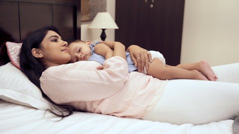 An affectionate Indian mother patting her little daughter to sleep at night. A pretty babysitter hugging cuddling a sweet girl child while lying down on the bed - improves immunity, sleep pattern...