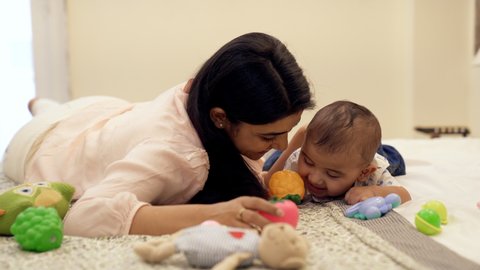 Single cheerful Indian mother playing with her young son - new parent, nuclear family, child care. A pretty female nurse and a sweet toddler playing with soft toys at home - trusted profession, bab...